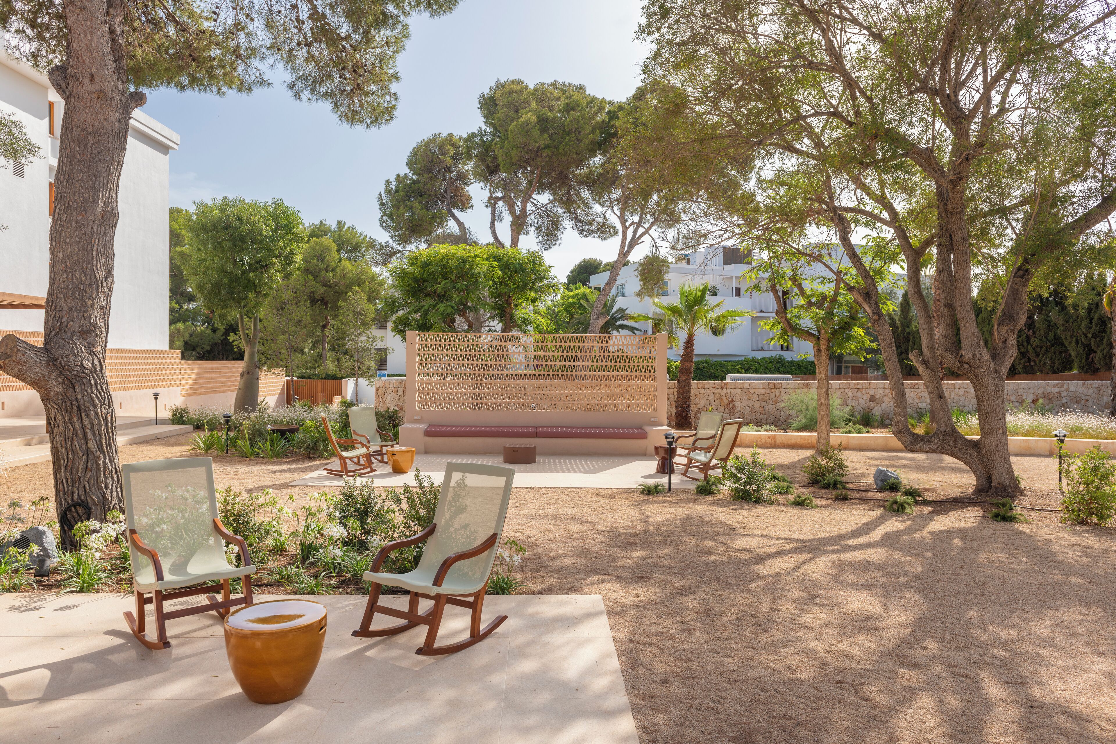 An outdoor seating area with chairs and a table, surrounded by trees and a white building.