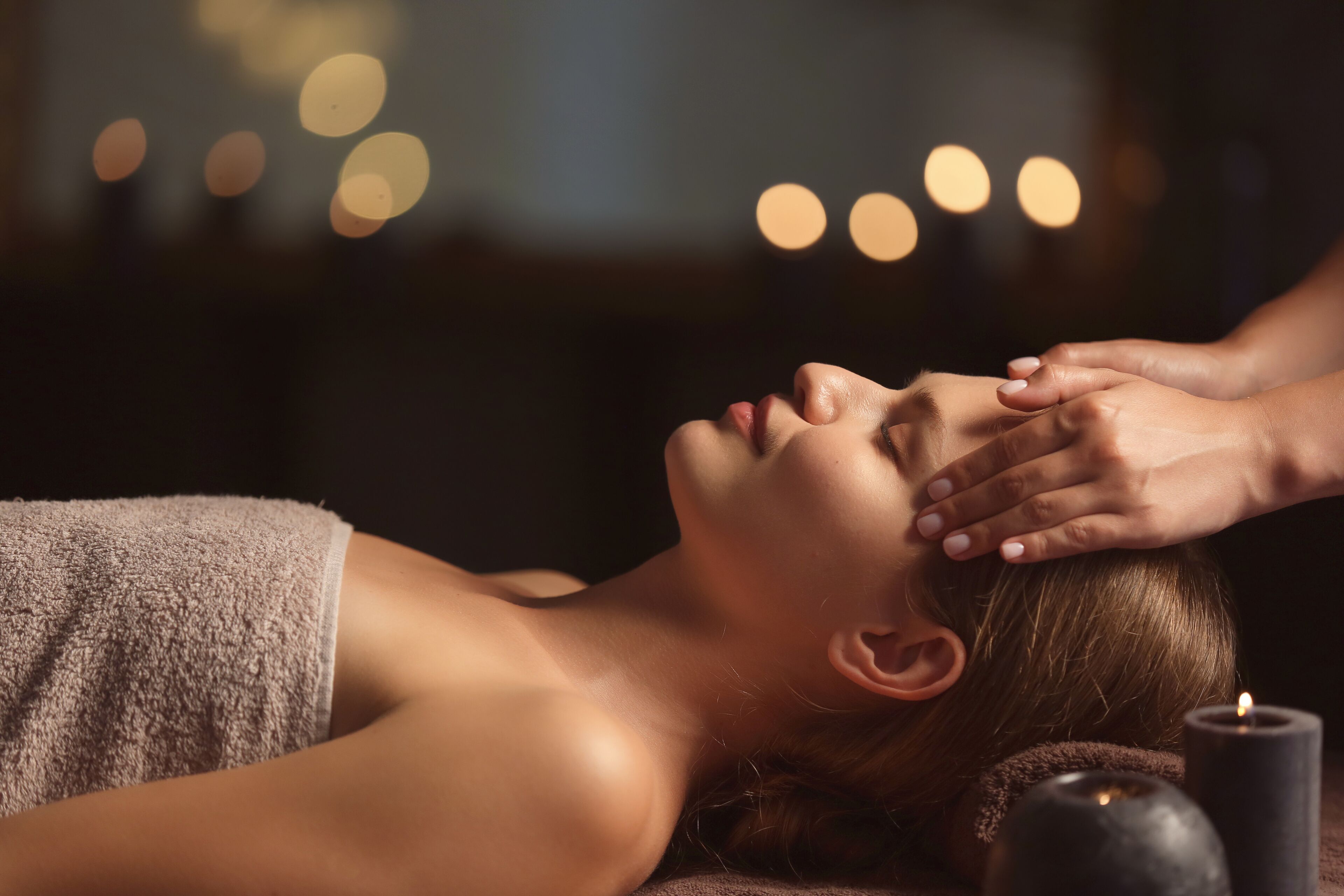 A person receiving a head massage with candles in the background.
