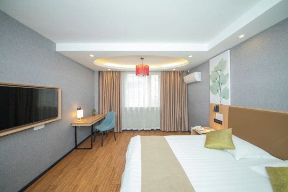Quarto de hotel com cama, escrivaninha, cadeira e televisão na parede.
