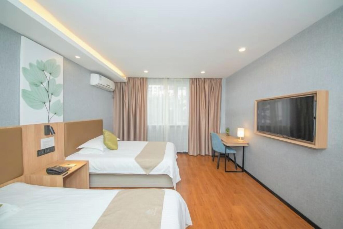 A hotel room with two beds, a desk, a chair, a TV, and a window with curtains.
