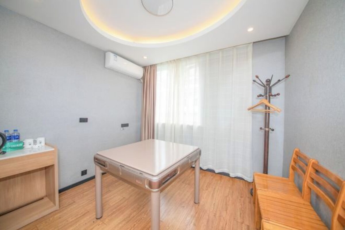 Quarto de hotel com mesa de madeira, um banco de madeira, um porta-casacos e uma janela com cortinas.