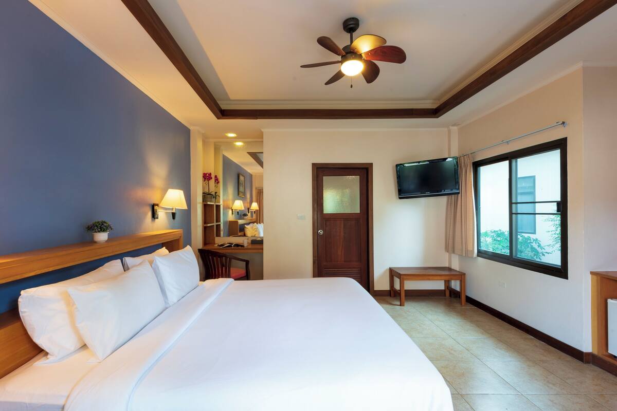 A hotel room with a large bed, a ceiling fan, a TV mounted on the wall, and a window with a view of the outside.