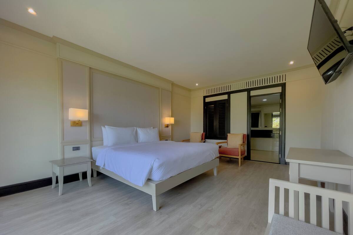 A hotel room with a large bed, bedside tables, a chair, a desk, and a TV mounted on the wall.