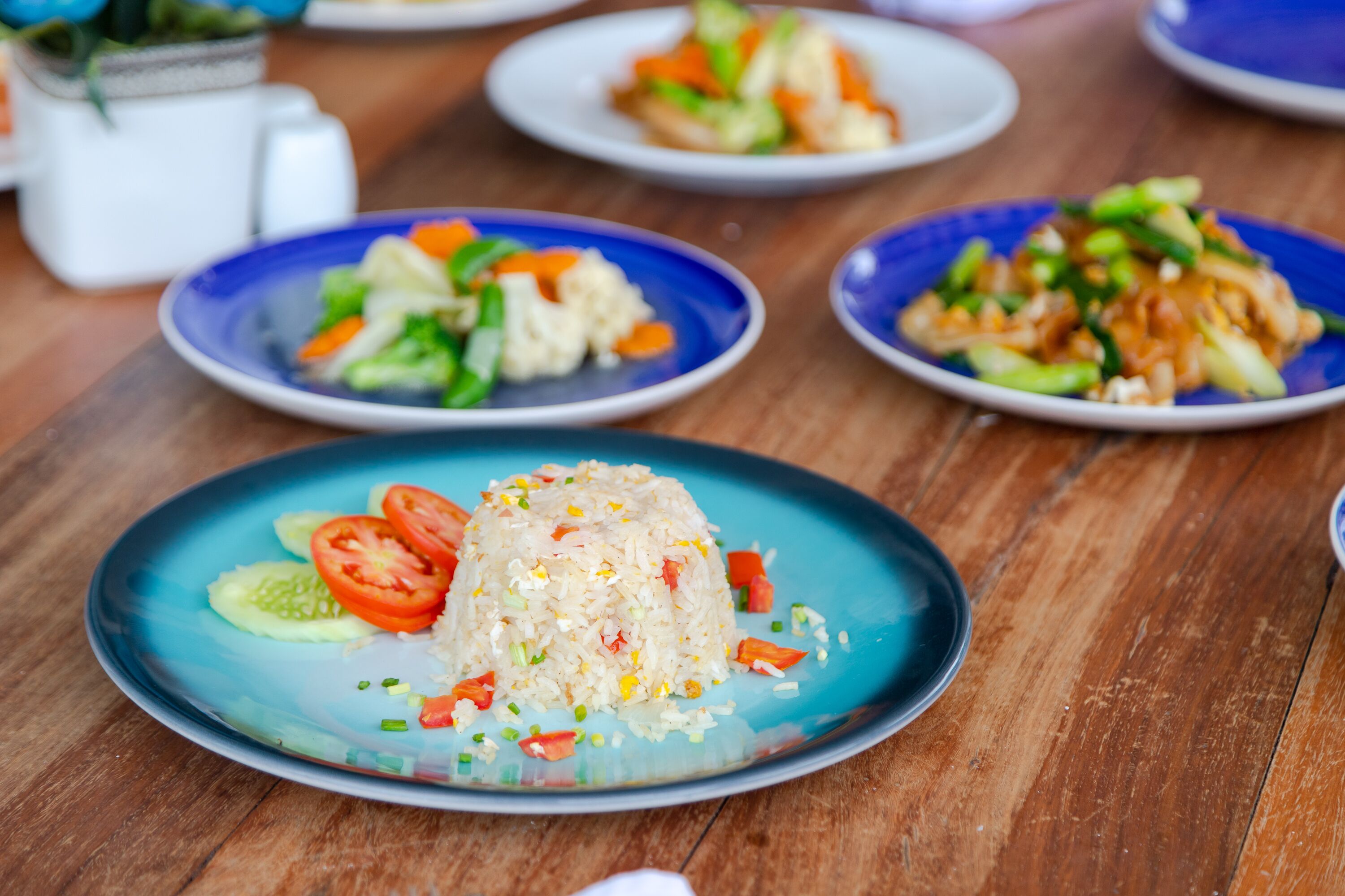 A table with various dishes, including a plate of fried rice with vegetables and a plate of stir-fried vegetables.