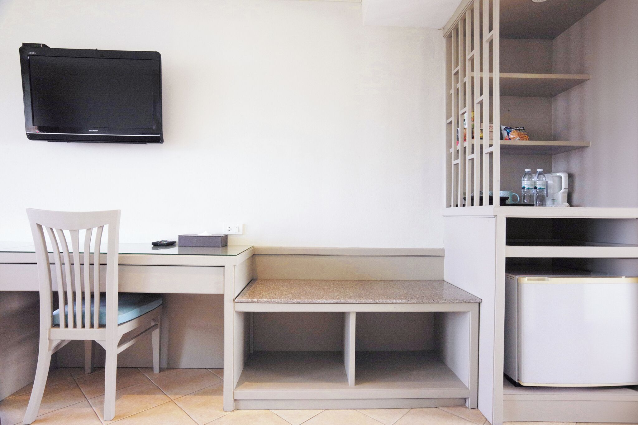A small, clean room with a desk, chair, TV, and a mini-fridge.