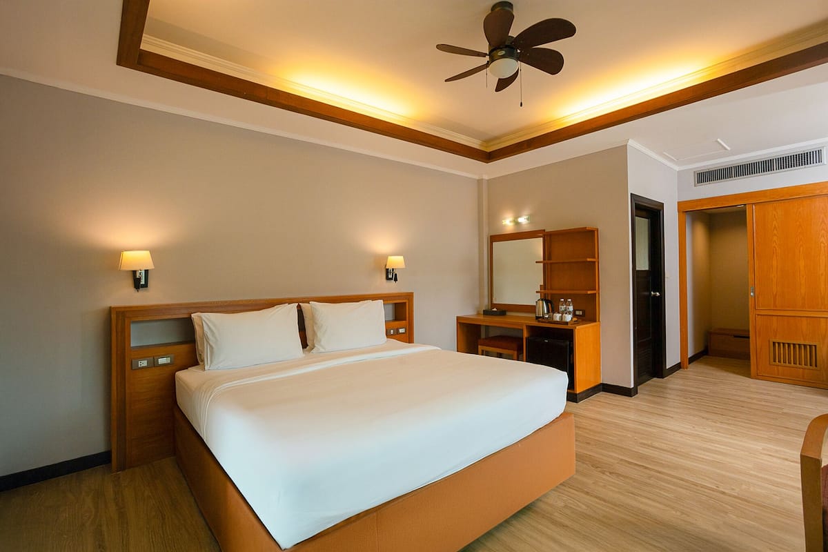 A hotel room with a large bed, bedside lamps, a ceiling fan, a desk with a chair, a wardrobe, and a mirror.