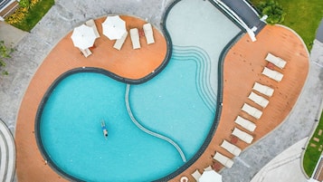Vista aérea de um resort com uma piscina grande, espreguiçadeiras e uma palmeira.