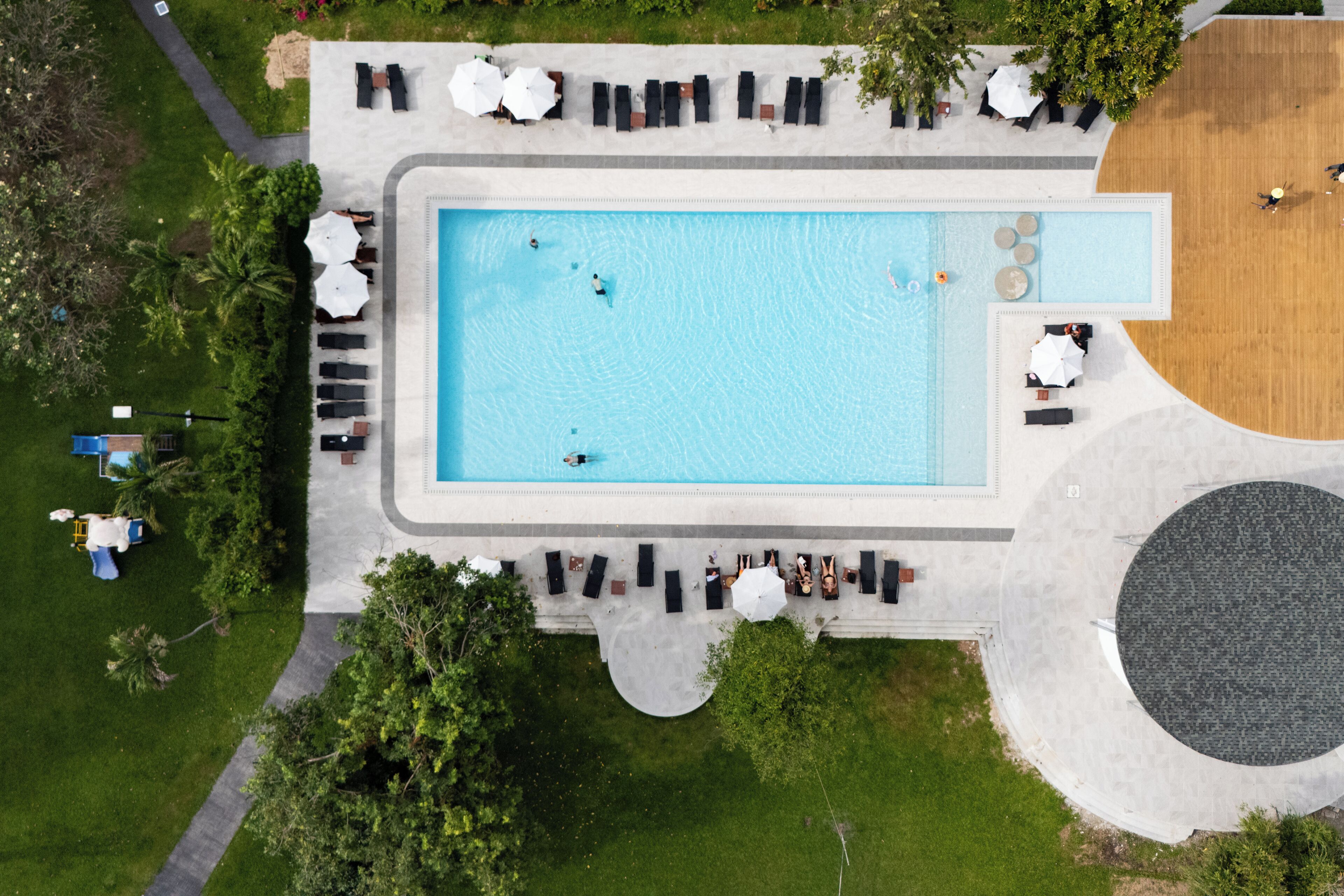 An aerial view of a swimming pool area with lounge chairs and umbrellas, surrounded by greenery.
