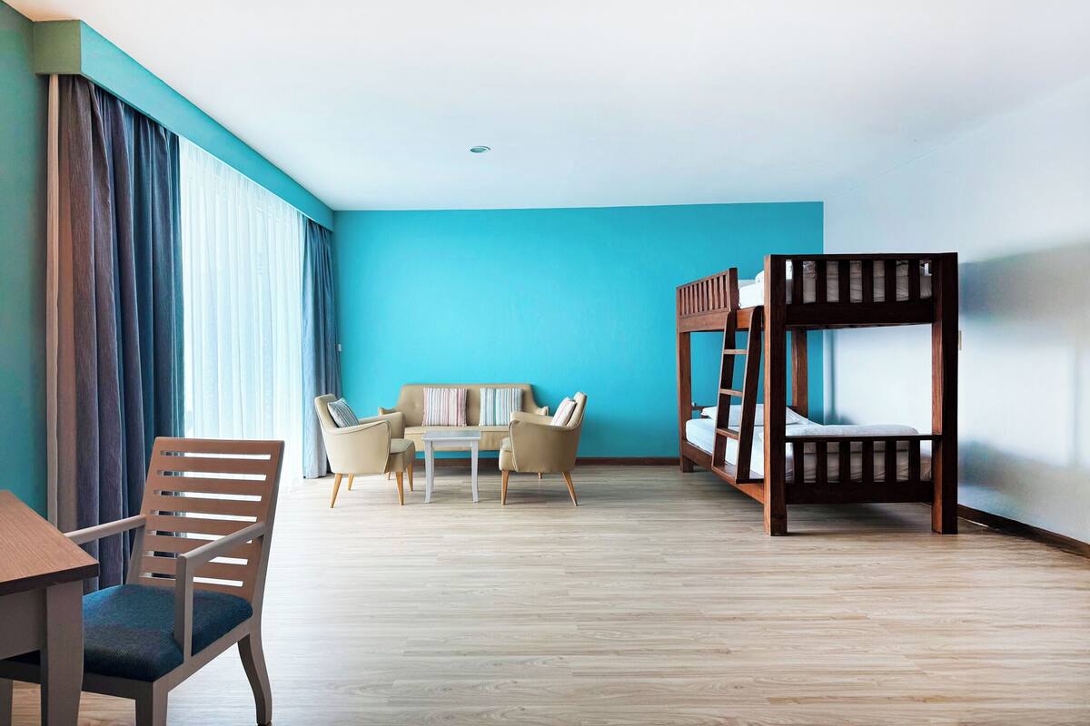 A hotel room with a wooden bunk bed, a sofa, a dining table with chairs, and a wooden desk.