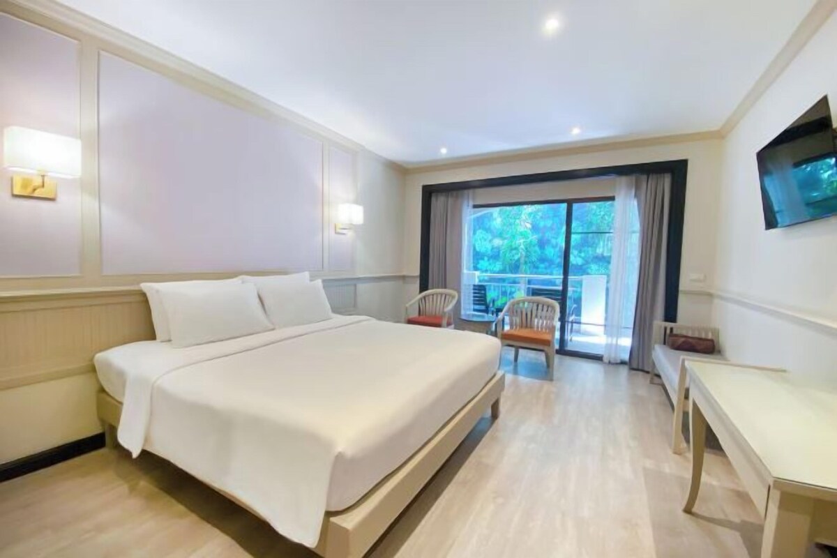 Habitación de hotel con cama, escritorio y silla. Hay un televisor montado en la pared y una ventana con cortinas.