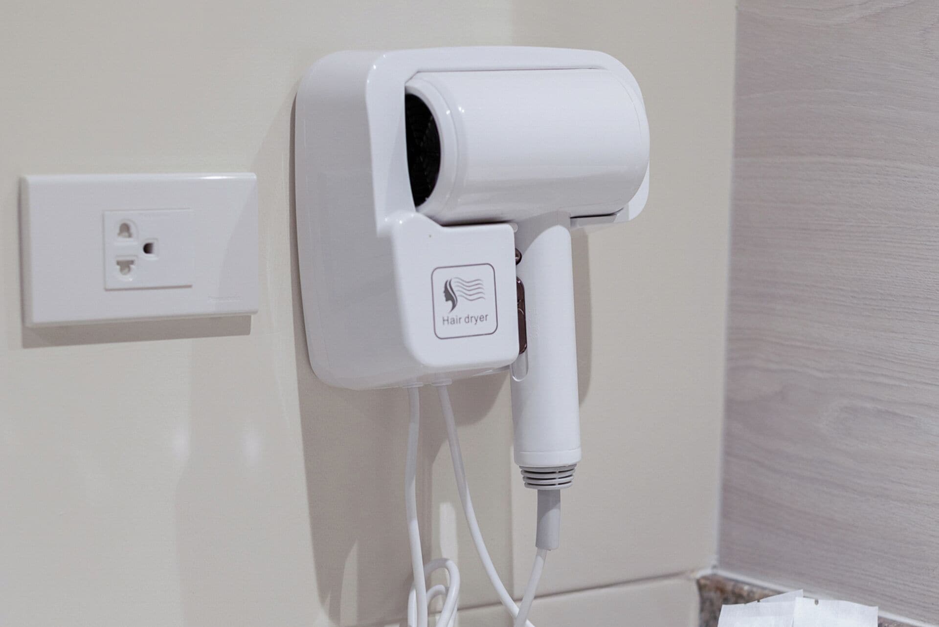 A hair dryer mounted on a wall with a power outlet nearby.