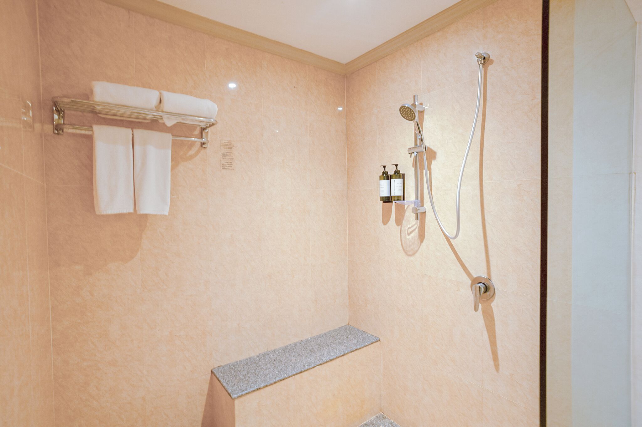A modern bathroom with a bench, a towel rack, and a shower unit.