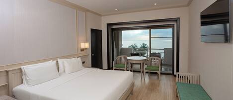 A hotel room with a large bed, a small table with chairs, a balcony with a table and chairs, and a TV mounted on the wall.