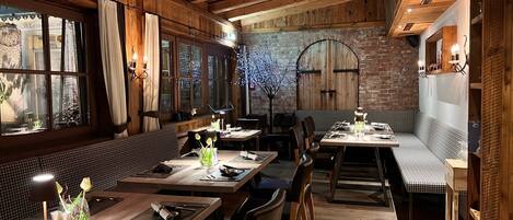 Een gezellig restaurant met houten inrichting, grote ramen en een bakstenen muur. Tafels zijn gedekt met bestek en glazen.