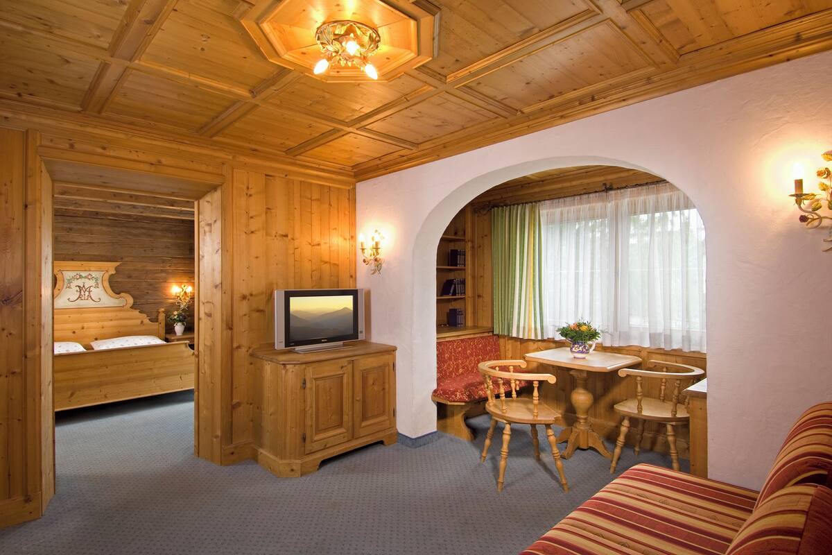 A wooden interior with a bed, TV, dining table, and chairs.