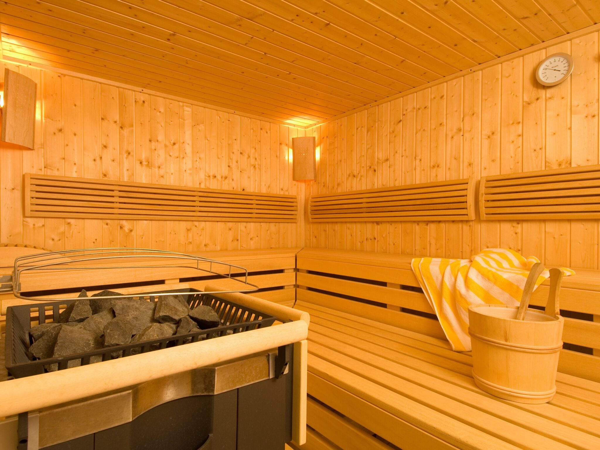 Een sauna met houten banken, een stenen warmtebron en een houten emmer.