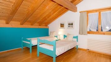 Quarto com teto de madeira, duas camas, janela com cortinas e radiador fixado na parede.
