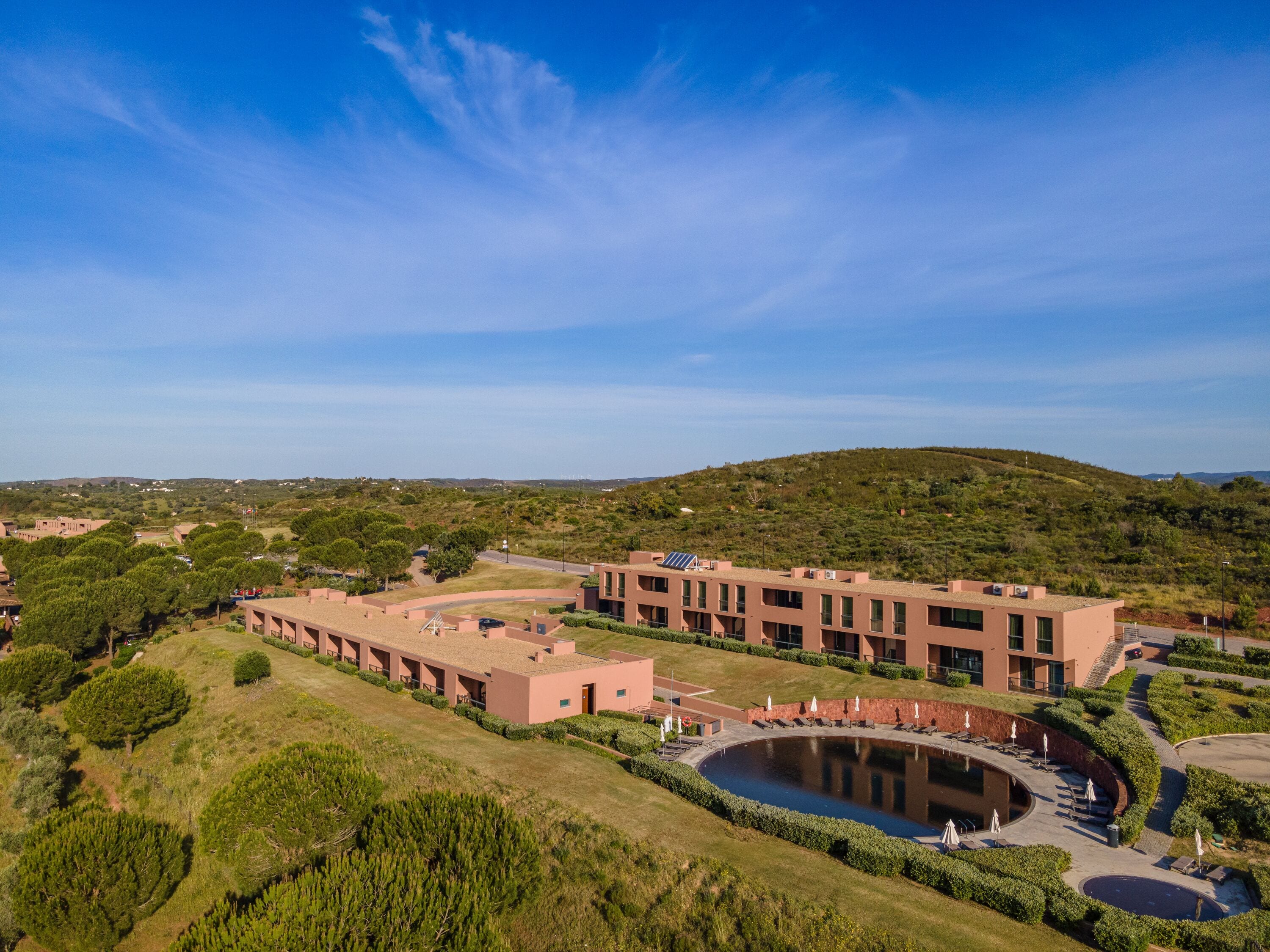 A modern building complex with a central courtyard, surrounded by greenery and hills.