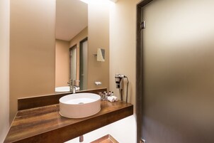 Un baño moderno con un lavabo redondo, un espejo grande y un secador de pelo en la encimera.