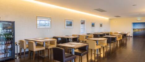 A restaurant with multiple tables and chairs, a refrigerator with bottles, and framed pictures on the wall.