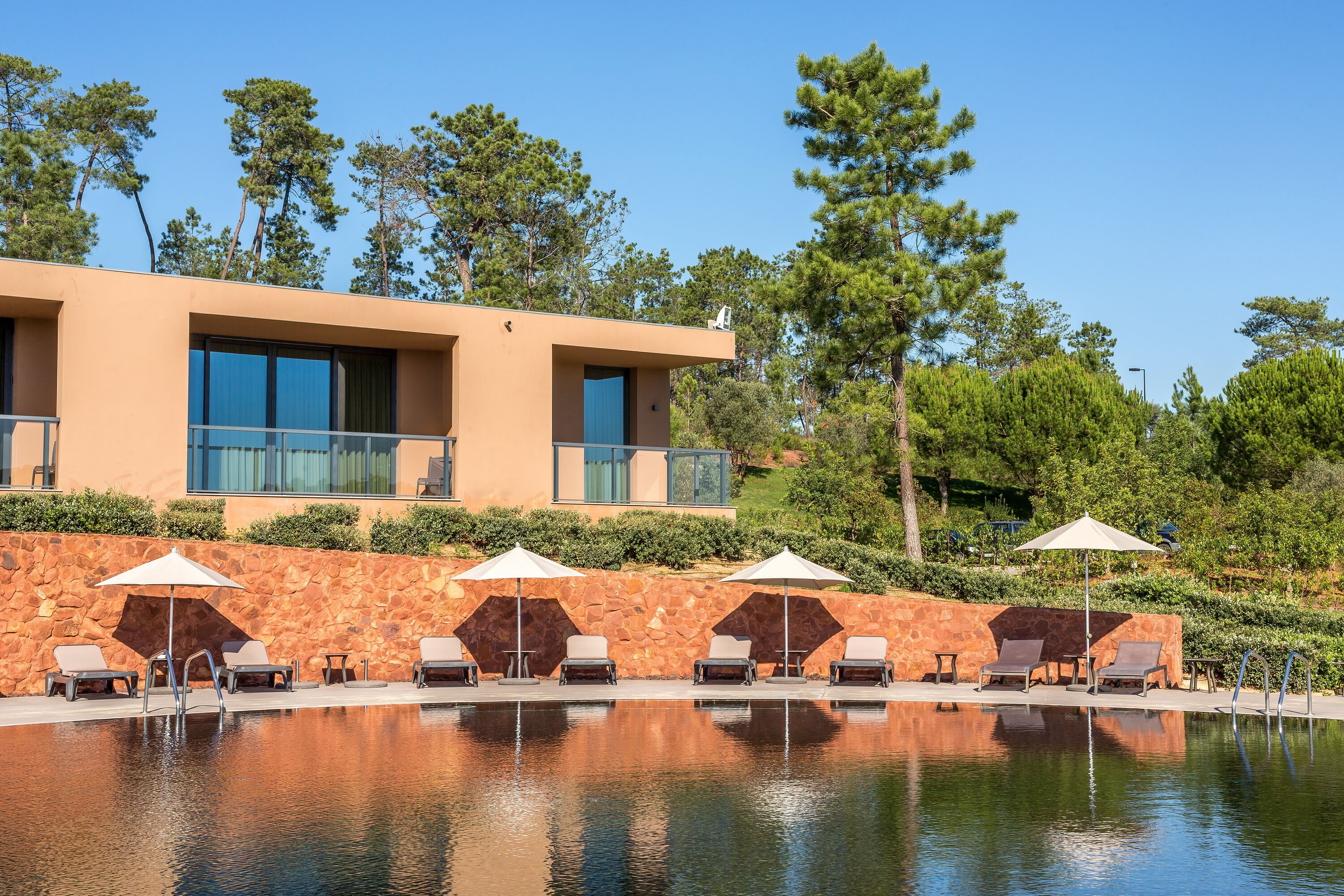 A modern hotel with a swimming pool, outdoor seating, and a stone wall.