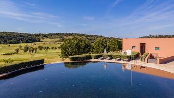 An infinity pool with a view of a golf course and a building with a staircase and a trash bin.