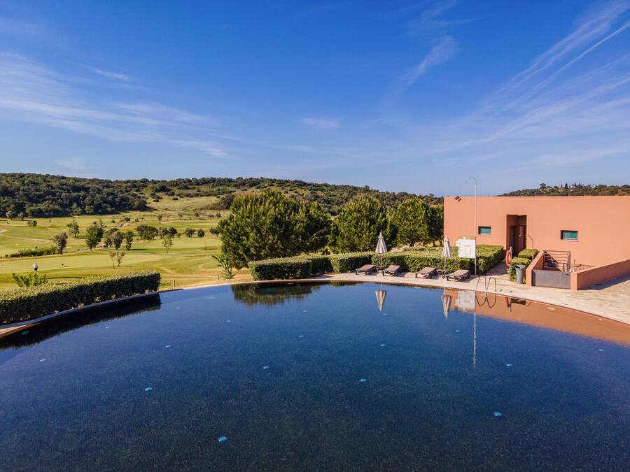 An infinity pool with a view of a golf course and a building with a staircase and a trash bin.