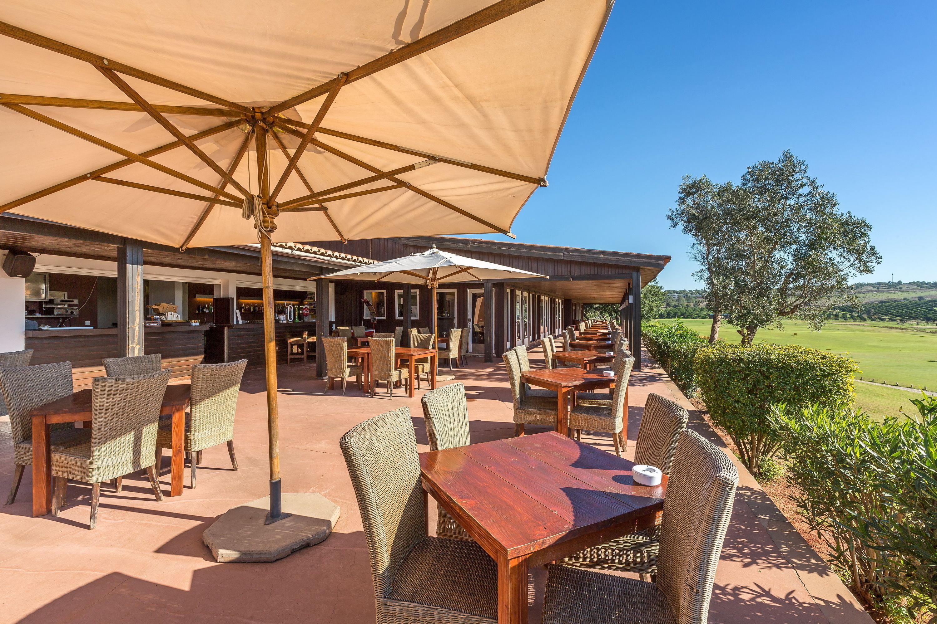 Un área de patio al aire libre con mobiliario de mimbre y sombrillas grandes, con vistas a un campo de golf.