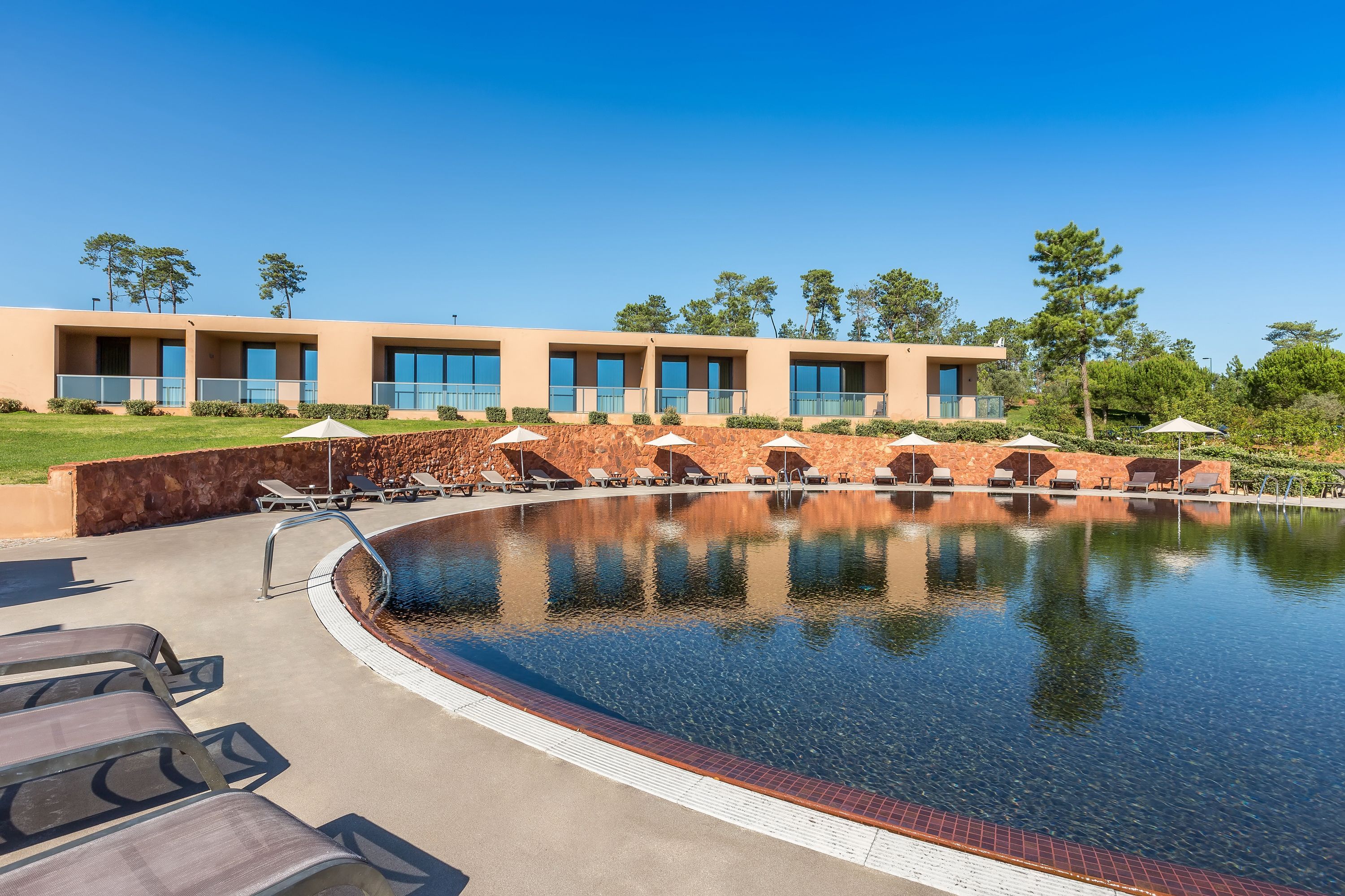 Un hotel moderno con piscina, lettini e un cielo azzurro limpido.