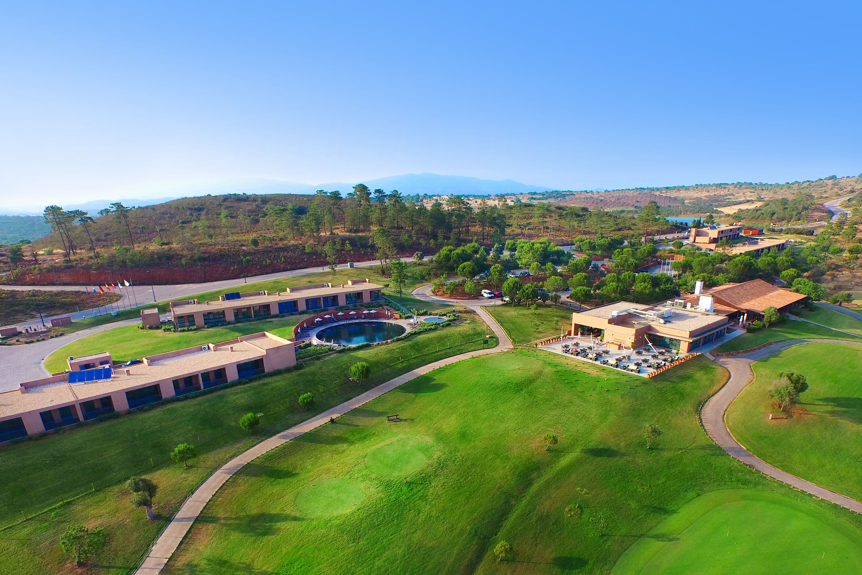 An aerial view of a resort with multiple buildings, a swimming pool, and a large green lawn.