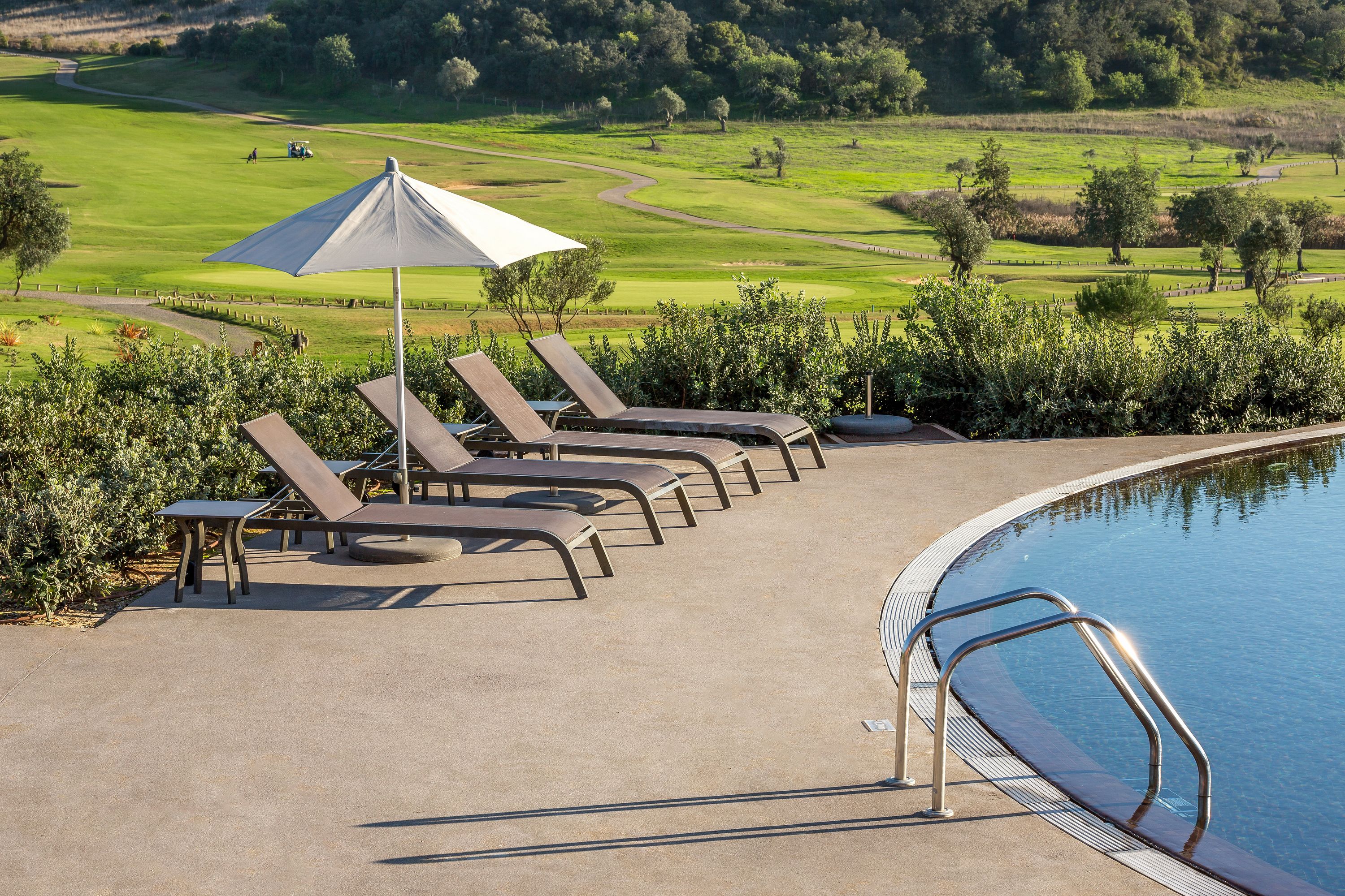 A poolside area with lounge chairs and a view of a golf course.