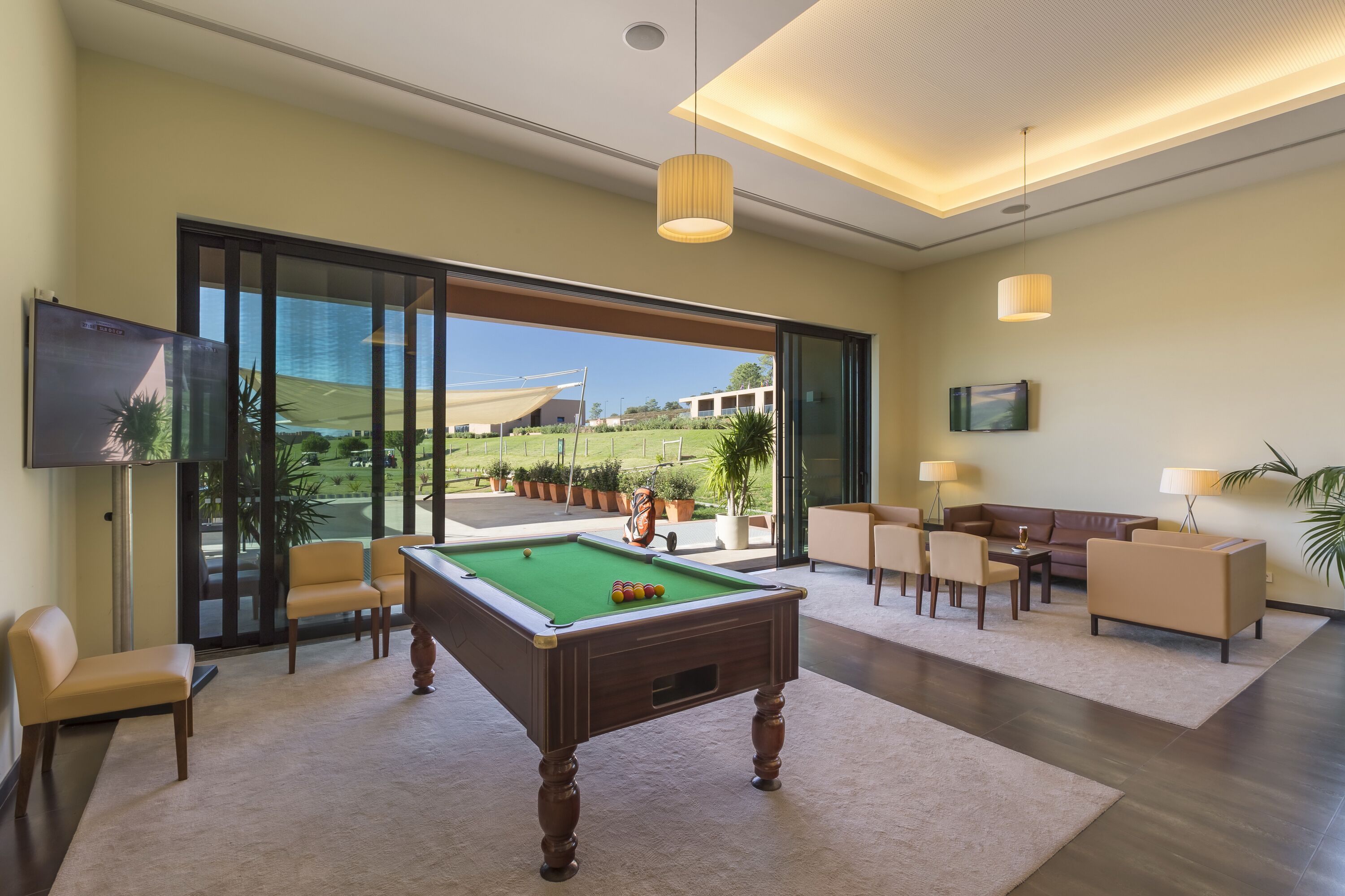 A modern indoor pool area with a pool table, comfortable seating, and large windows offering a view of the outdoors.