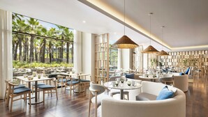 A spacious indoor dining area with wooden tables and chairs, large windows with a view of palm trees, and hanging wicker lamps. - Algarve Marriott Salgados Golf Resort & Spa (Albufeira)