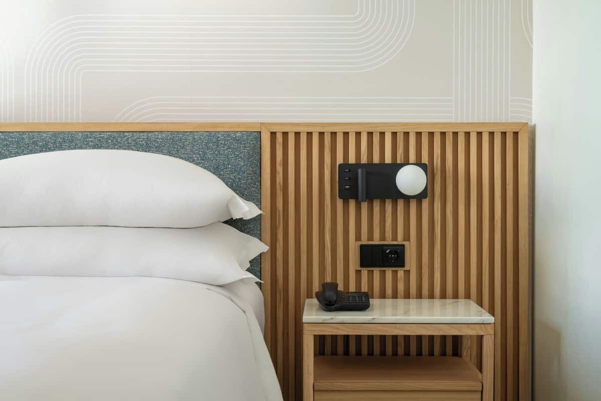 Una habitación de hotel con una cama, una mesita de noche con teléfono y un altavoz en la pared.