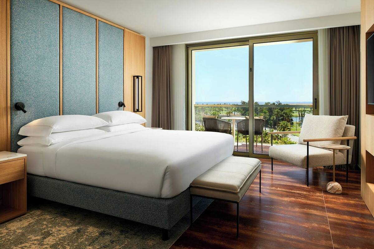 Una habitación de hotel moderna con una cama grande, un área de descanso con vistas y un balcón.