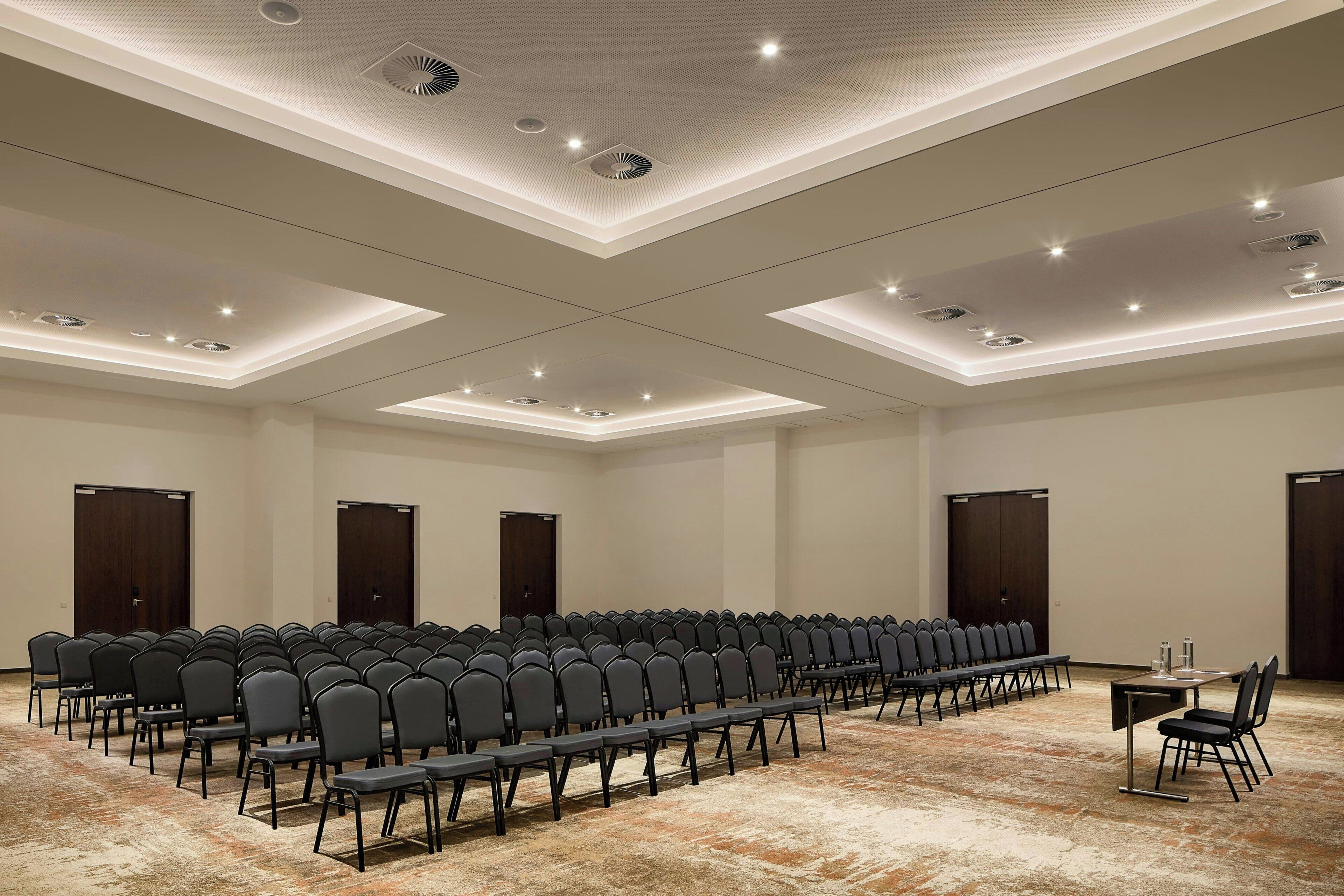 A conference room with rows of chairs, a long table, and a carpeted floor.