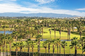 A golf course with palm trees, a pond, and distant mountains.
