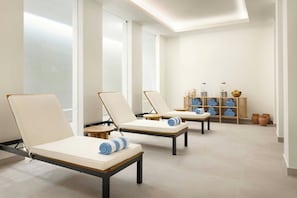 A spa area with three lounge chairs, a small table, and a shelf with towels and toiletries.