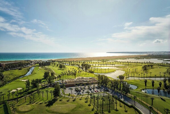 A golf course with a clubhouse, palm trees, and a view of the ocean.