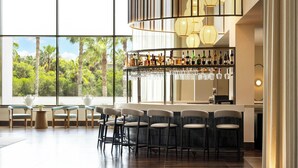 A modern bar area with a view of palm trees through large windows, bar stools, and a variety of bottles and glasses on the shelves. - Algarve Marriott Salgados Golf Resort & Spa (Albufeira)