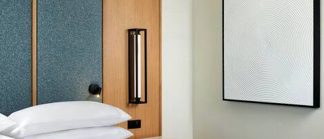 A modern hotel room with a neatly made bed, a wall-mounted artwork, and a wooden panel design.