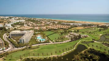 A golf course with a large building complex and a beach in the background.
