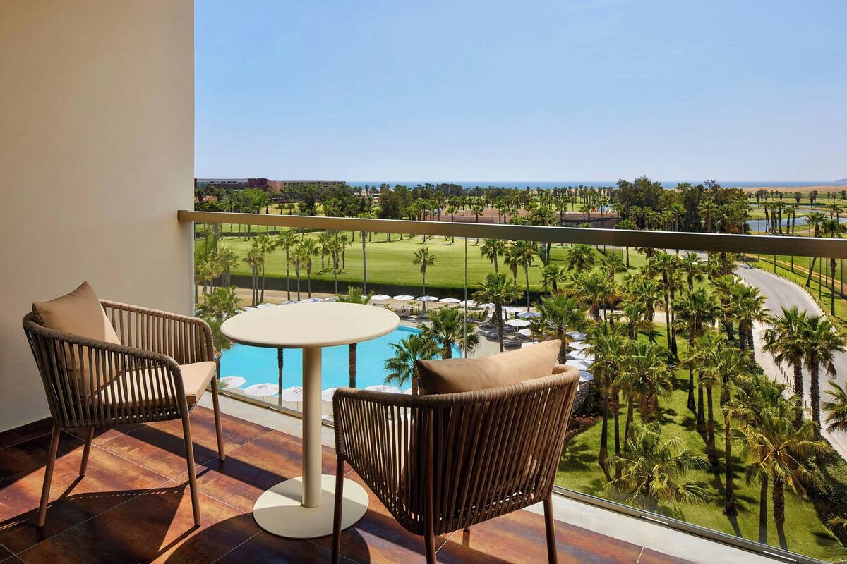 Un balcón con sillas de mimbre y una mesa redonda, con vista a una piscina y un campo de golf.