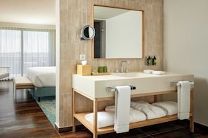 A modern hotel bathroom with a large mirror, a white sink, and a wooden vanity.