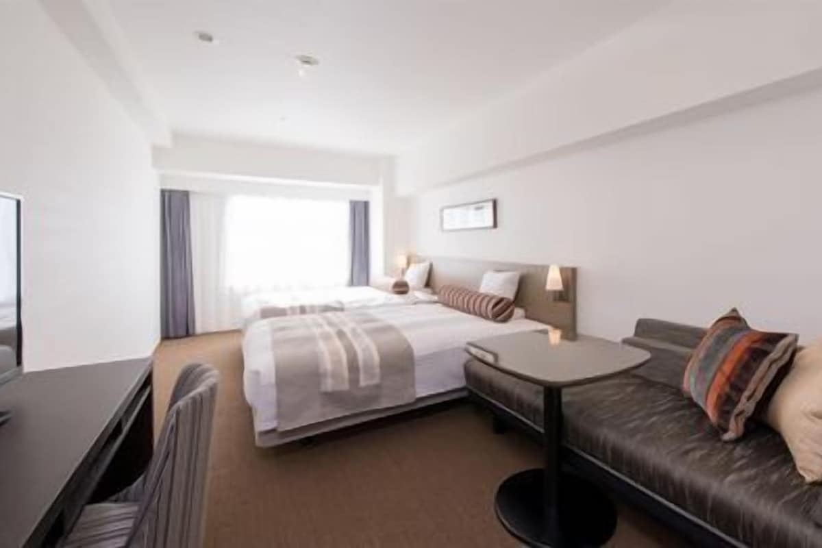 A hotel room with a bed, a sofa, a desk, and a TV.