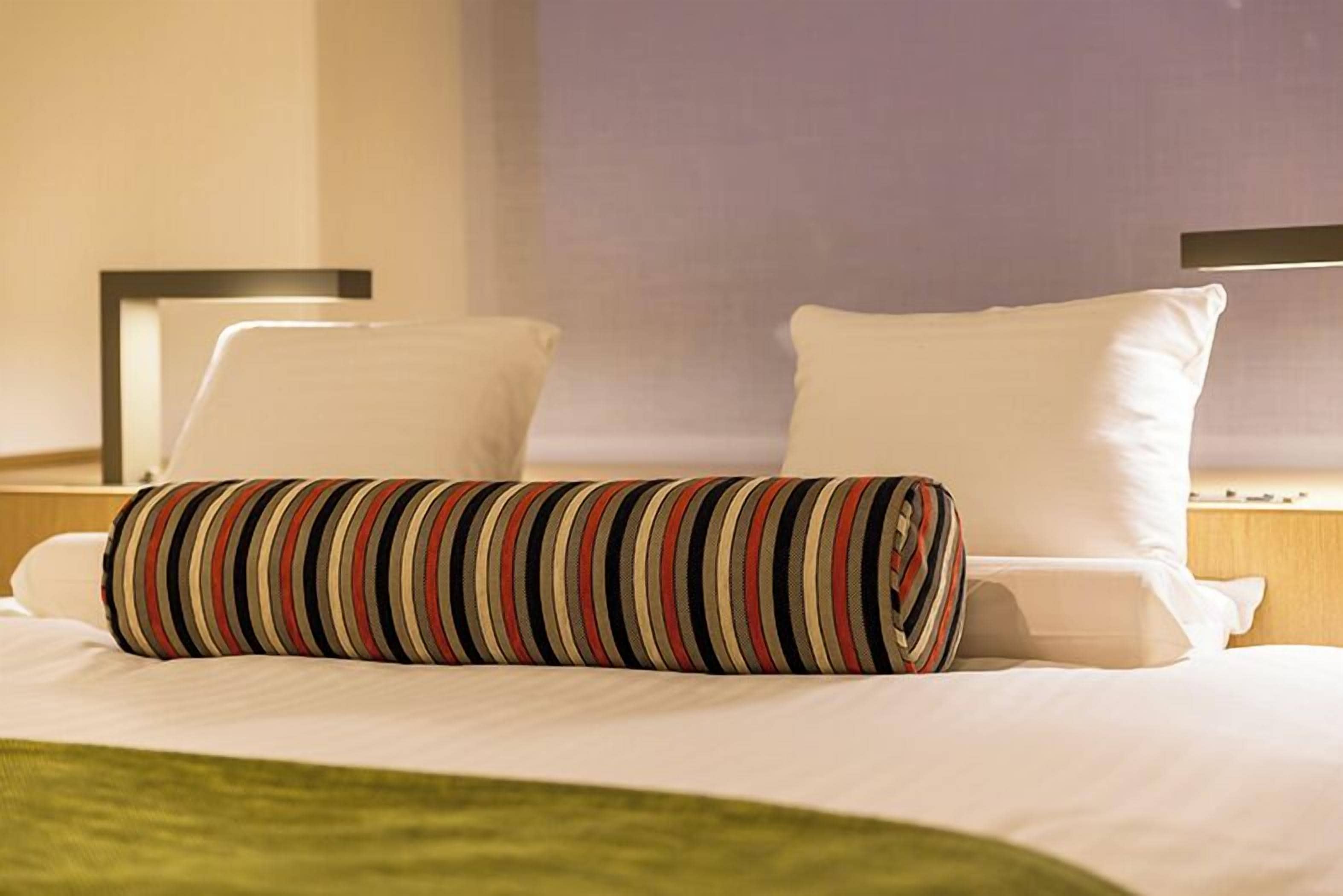 Une chambre d’hôtel avec un lit bien fait, deux oreillers et un coussin décoratif à rayures.