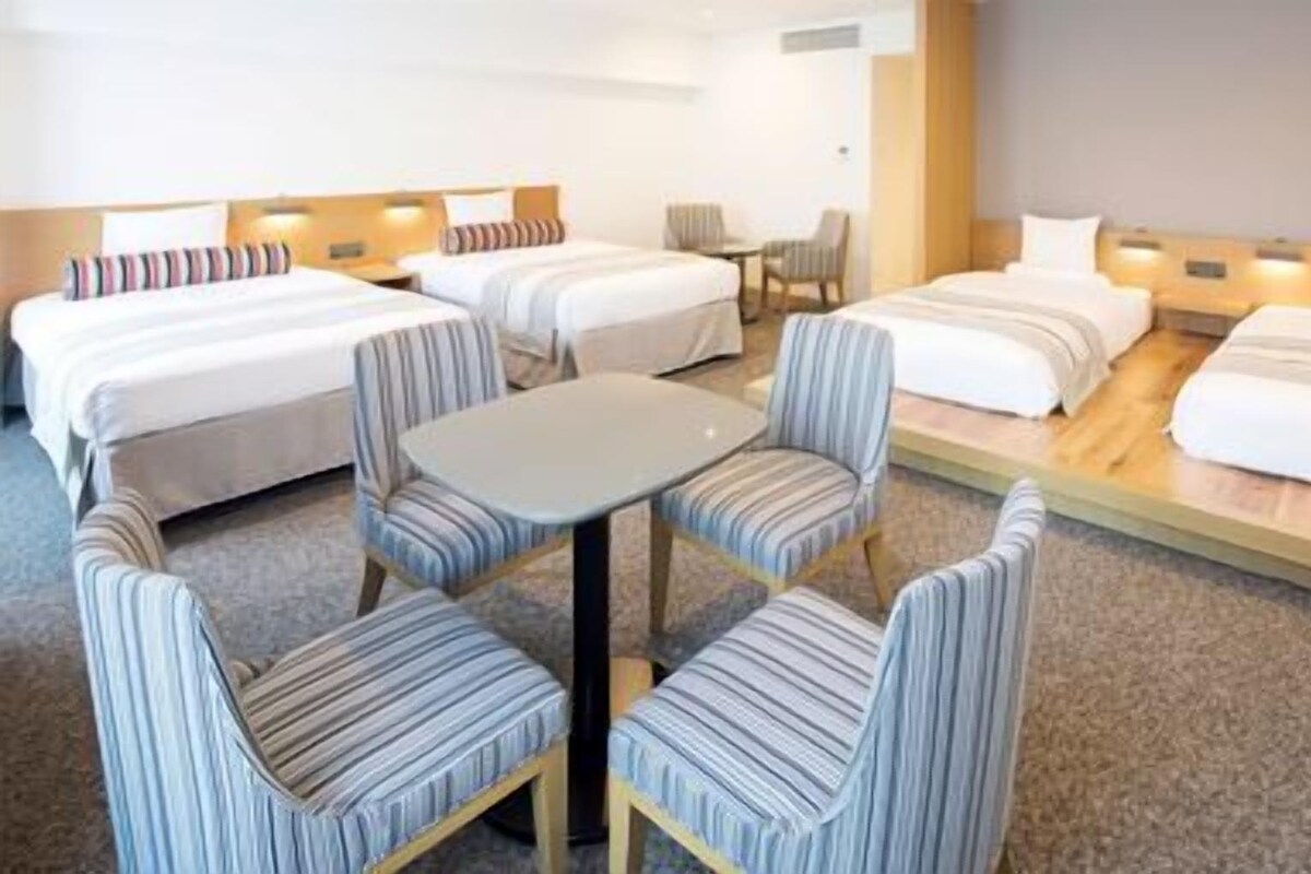 A hotel room with two beds, a small table, and striped chairs.