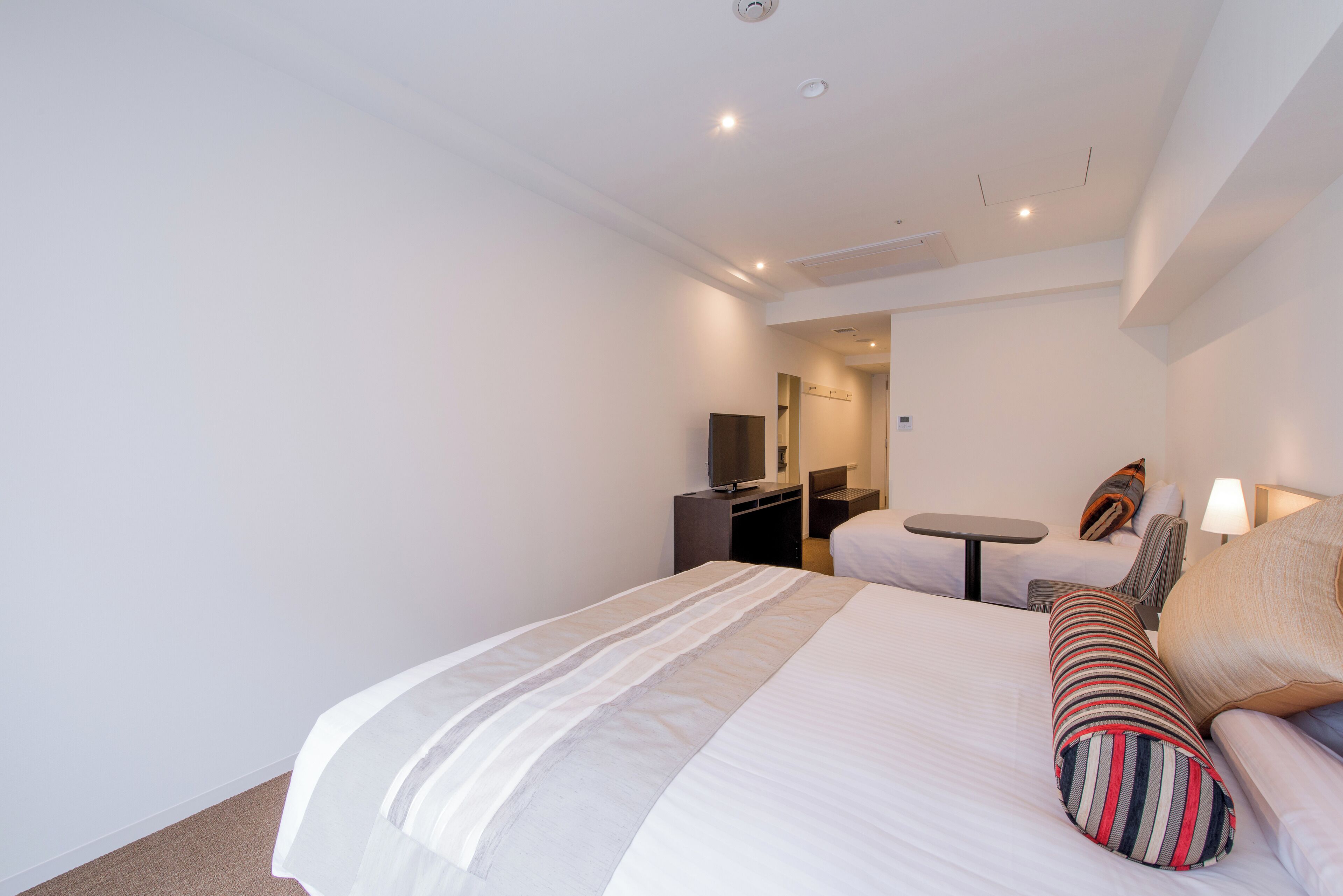 A hotel room with a large bed, a small desk, a chair, a TV, and a lamp.