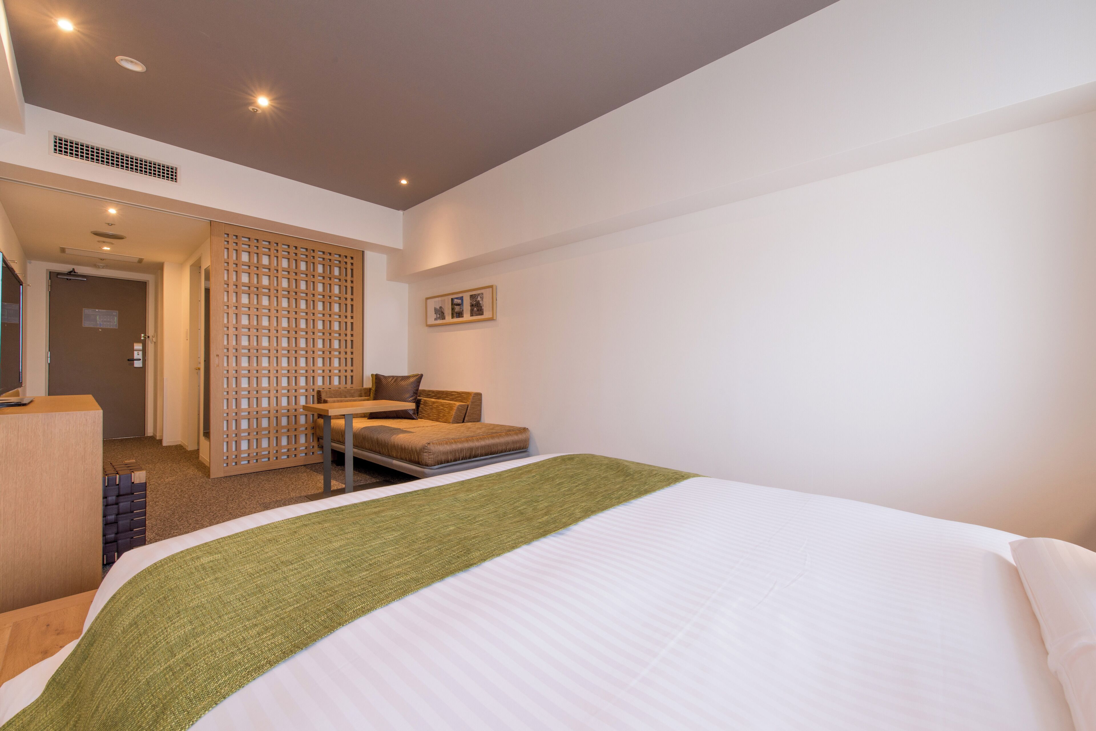 A hotel room with a bed, a desk, a chair, and a partition wall.