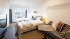 A hotel room with two beds, a sofa, a small table, and a TV.